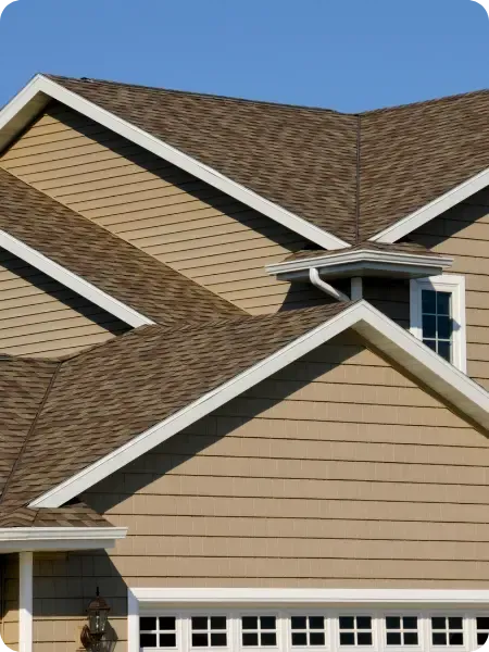 A close-up view of a residential roof in Ottawa with tan siding and a brown shingled roof against a clear blue sky.