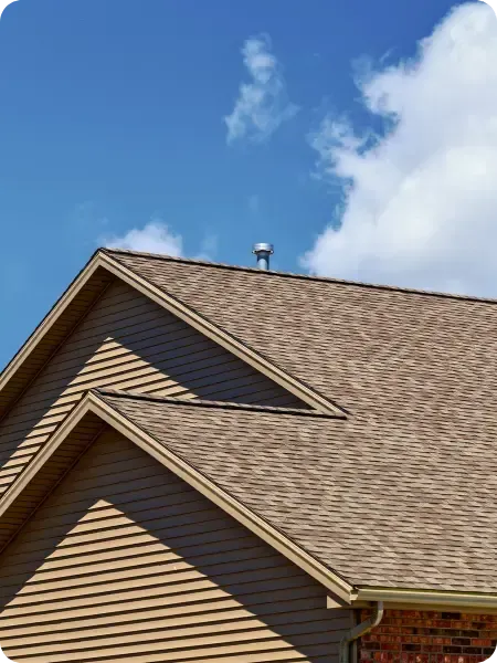 A newly replaced brown asphalt shingled roof against a blue sky with white clouds. A small metal vent pipe protrudes from the roof peak.