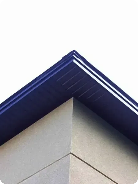 A close-up view of a newly replaced dark blue soffit and fascia detail on the corner of a house with beige siding