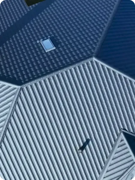 An aerial view of a metal roof with dark gray shingles and lighter gray ribbed metal sections, featuring a skylight and casting shadows.