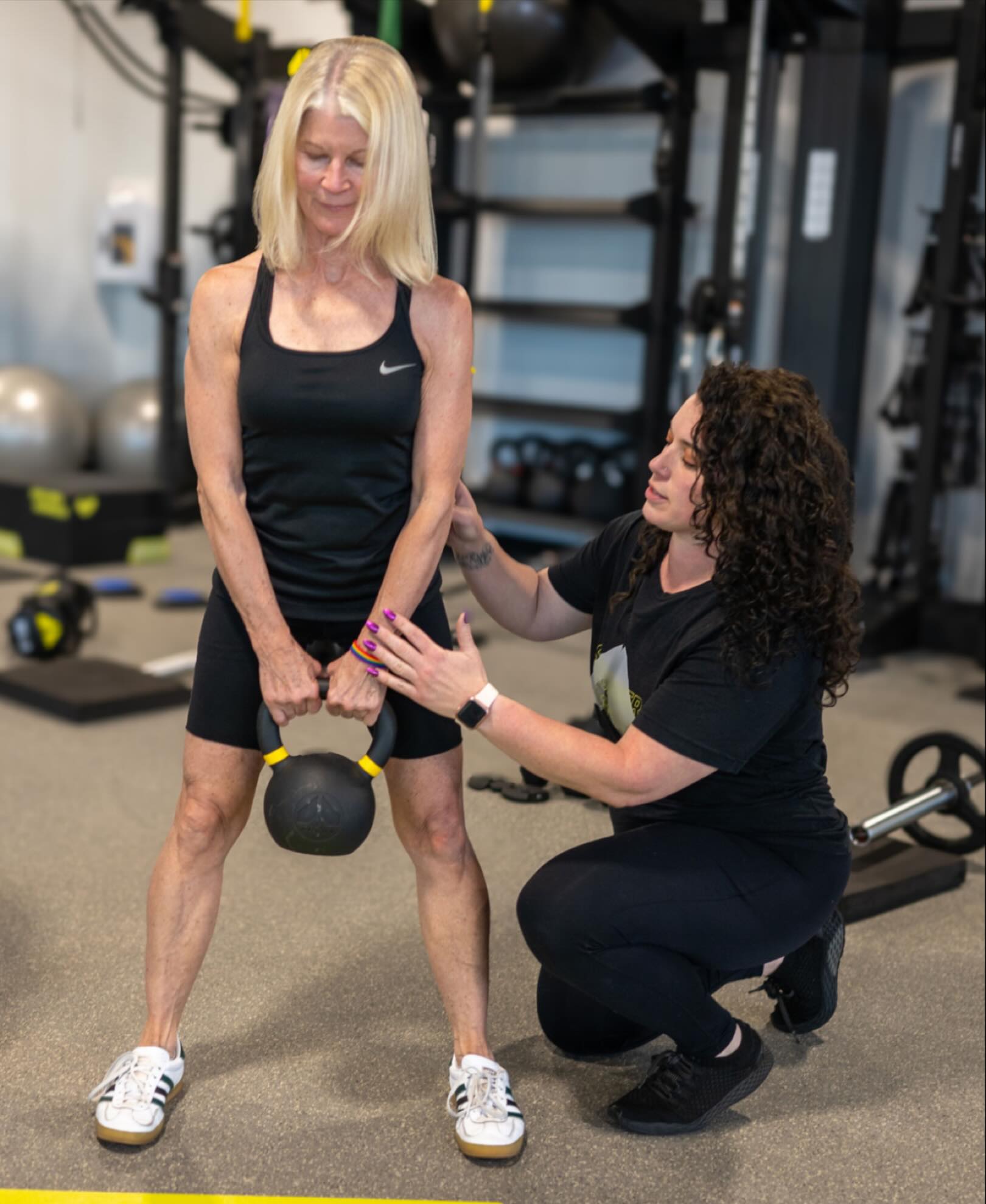 Personal trainer assisting older adult with kettlebell strength training exercise in fitness studio in Royal Oak MI focused on functional strength and mobility