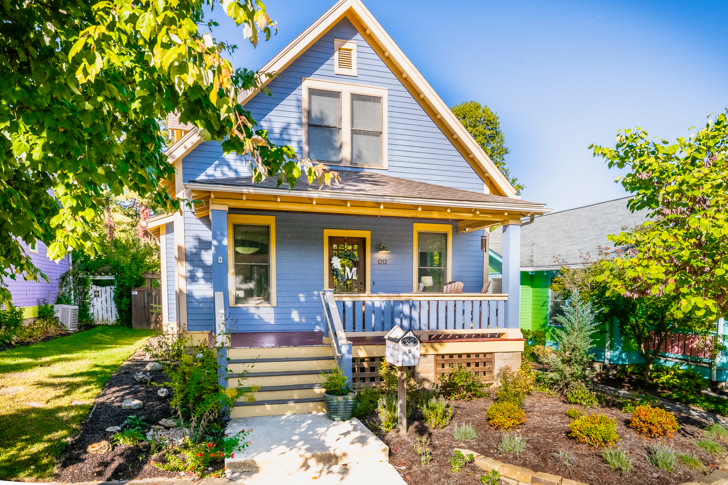 Blue Bloomington Indiana home with front porch, mature trees, and landscaped yard ready to sell