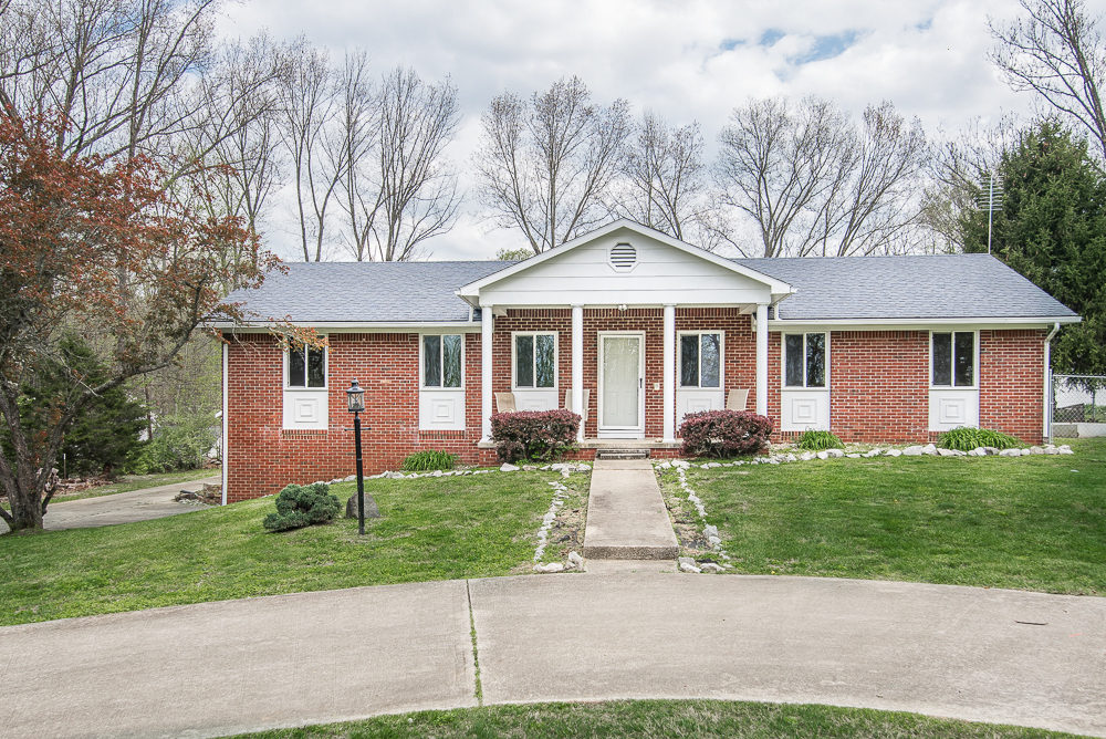 Red brick ranch home in Bedford, Indiana with white trim, covered front entry, landscaped walkway, and mature trees in the background.