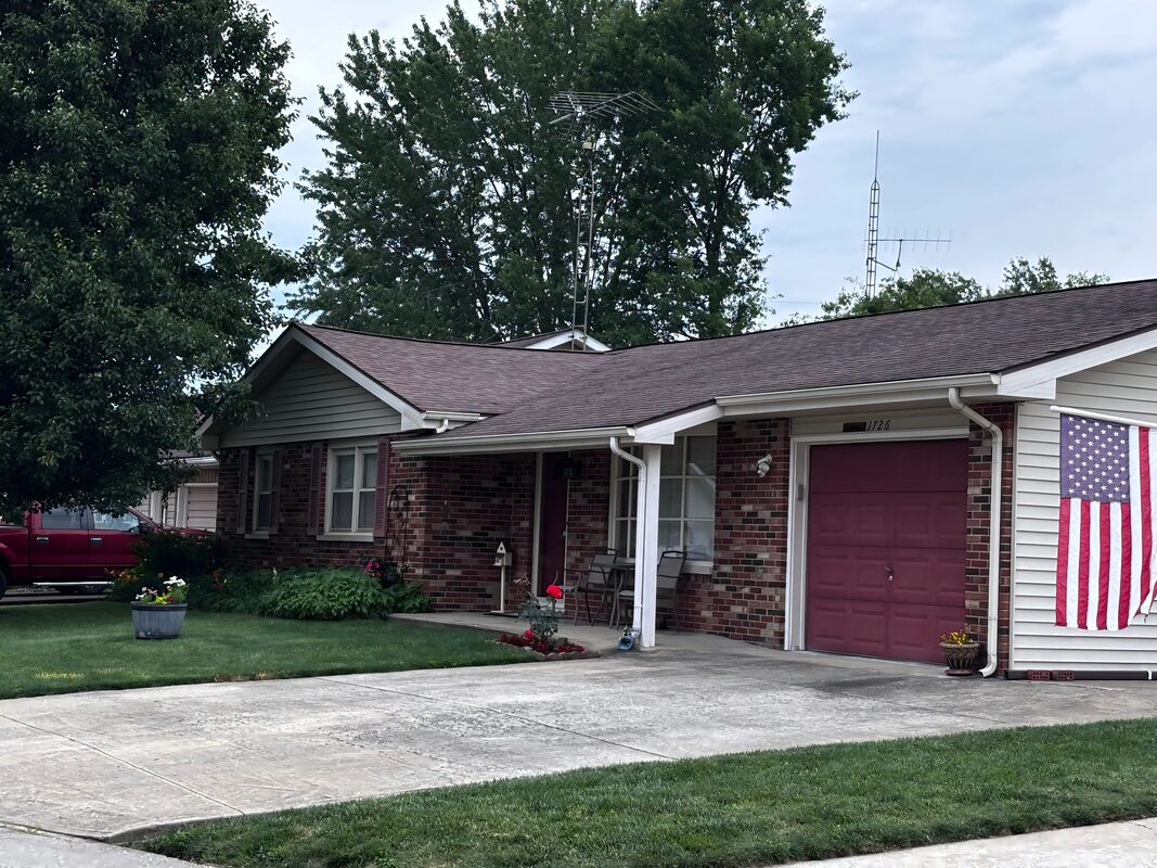 Brick ranch home with covered front porch, attached garage, and American flag displayed on a Bedford Indiana residential street