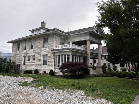 Historic two-story limestone home in Bedford Indiana with covered front porch and mature landscaping