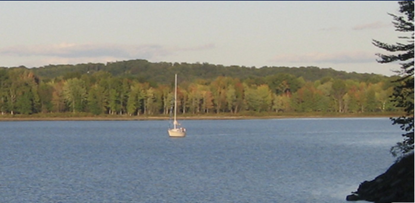 Sailboat anchored on Lake Monroe with calm blue water, wooded shoreline, and rolling hills in the background.