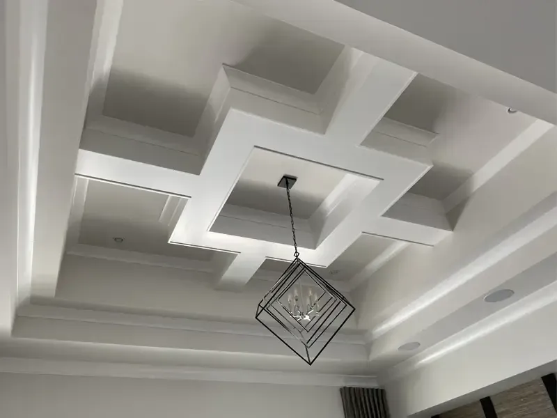 Master-level finish carpentry: A custom geometric white coffered ceiling with modern chandelier and recessed lighting, professionally installed by Brothers Home Group in Naples, FL