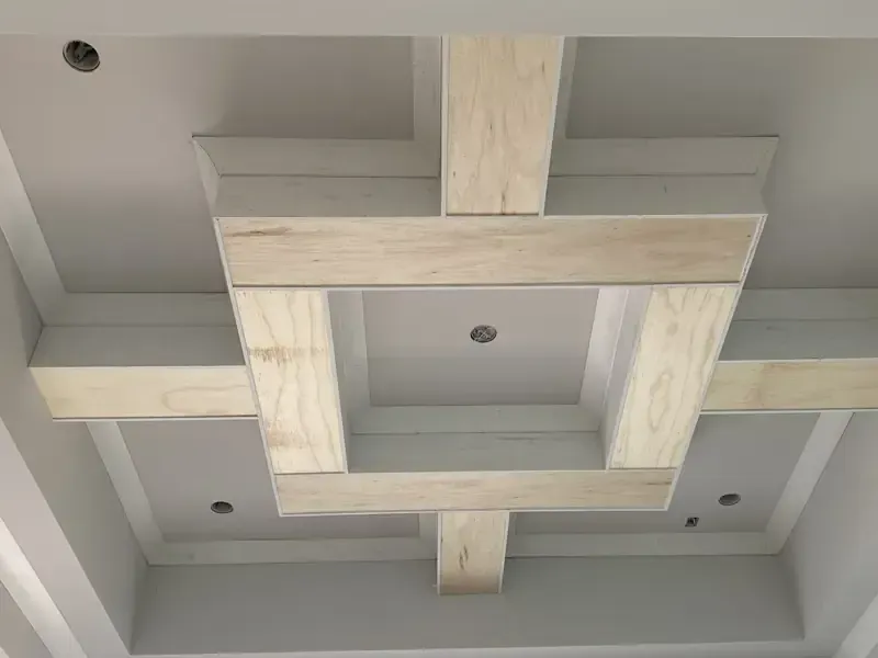 Masterly construction details of a detailed custom coffered tray ceiling under construction, showcasing the raw plywood finish beams and early-stage luxury finish carpentry work by Brothers Home Group in Naples, FL.