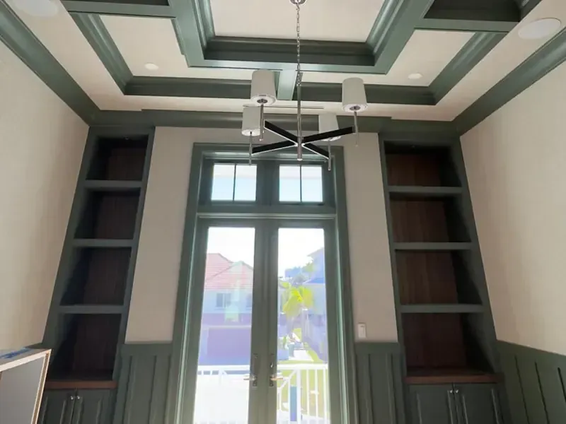 Custom sage green coffered ceiling with matching built-in bookshelves and wainscoting, handcrafted by Brothers Home Group in a luxury Naples home.