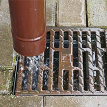 Rainwater flowing into a stormwater drain grate designed to collect surface runoff.