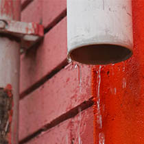 Water dripping from a residential downpipe indicating potential stormwater drainage problems.