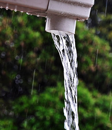 Rainwater flowing freely from a residential downpipe during a storm.