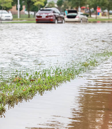 Surface water pooling across a grass verge and roadway due to inadequate stormwater drainage.