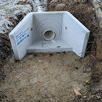 Newly installed stormwater drainage pit connected to underground pipework in a trench.