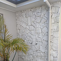 White stormwater downpipe securely mounted against an exterior stone wall.