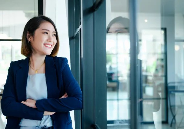 Focused businesswoman gazing out of office window, reflecting determination and strategic thinking for HR and M&A success.