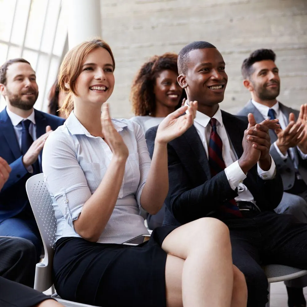 Diverse M&A professionals applauding at Boston Summit, celebrating breakthrough insights and meaningful connections that drive successful merger outcomes with limited seating for personalized attention