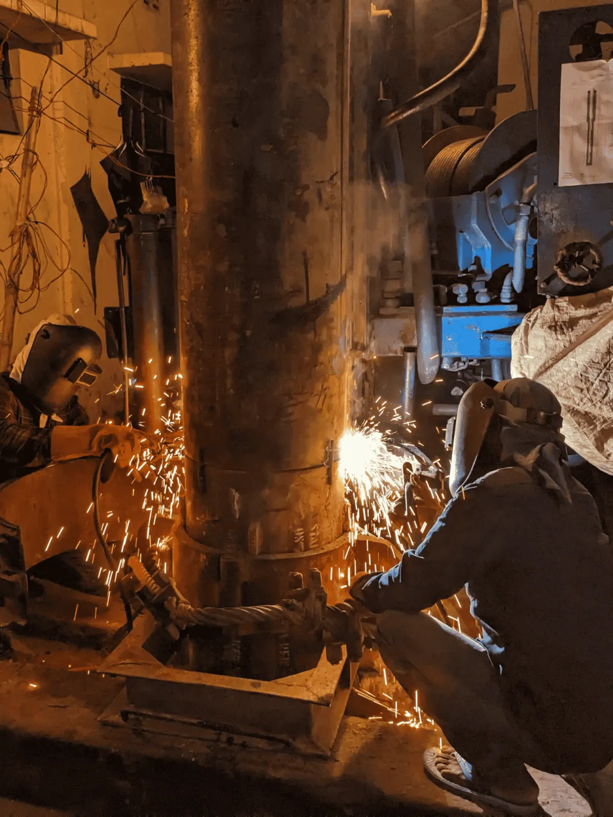 Two welders in protective gear work on a large metal column during power plant welding in Utah