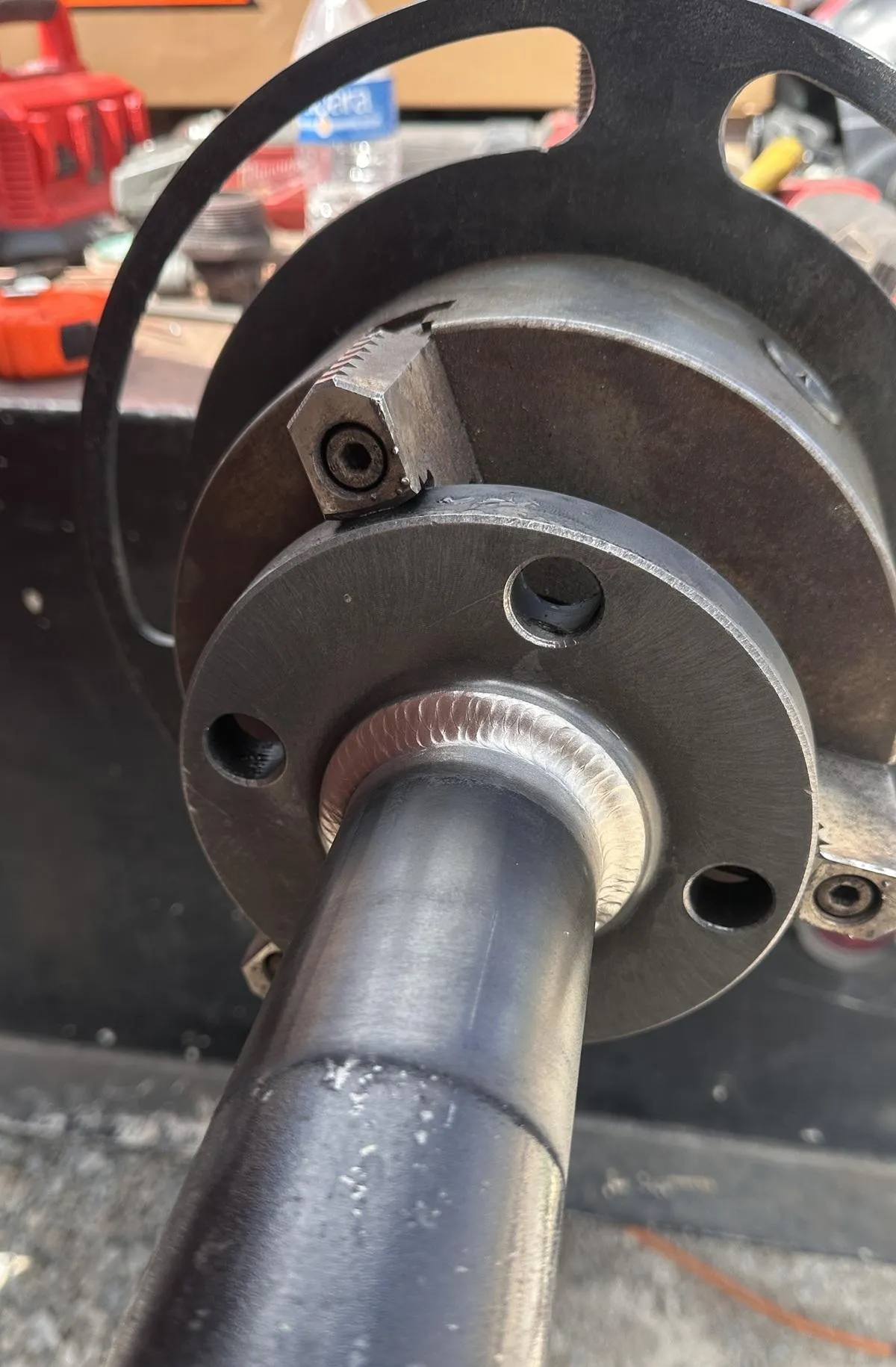 Metal mechanical part in industrial fabrication, showing a cylindrical shaft on a flanged base with bolt holes.