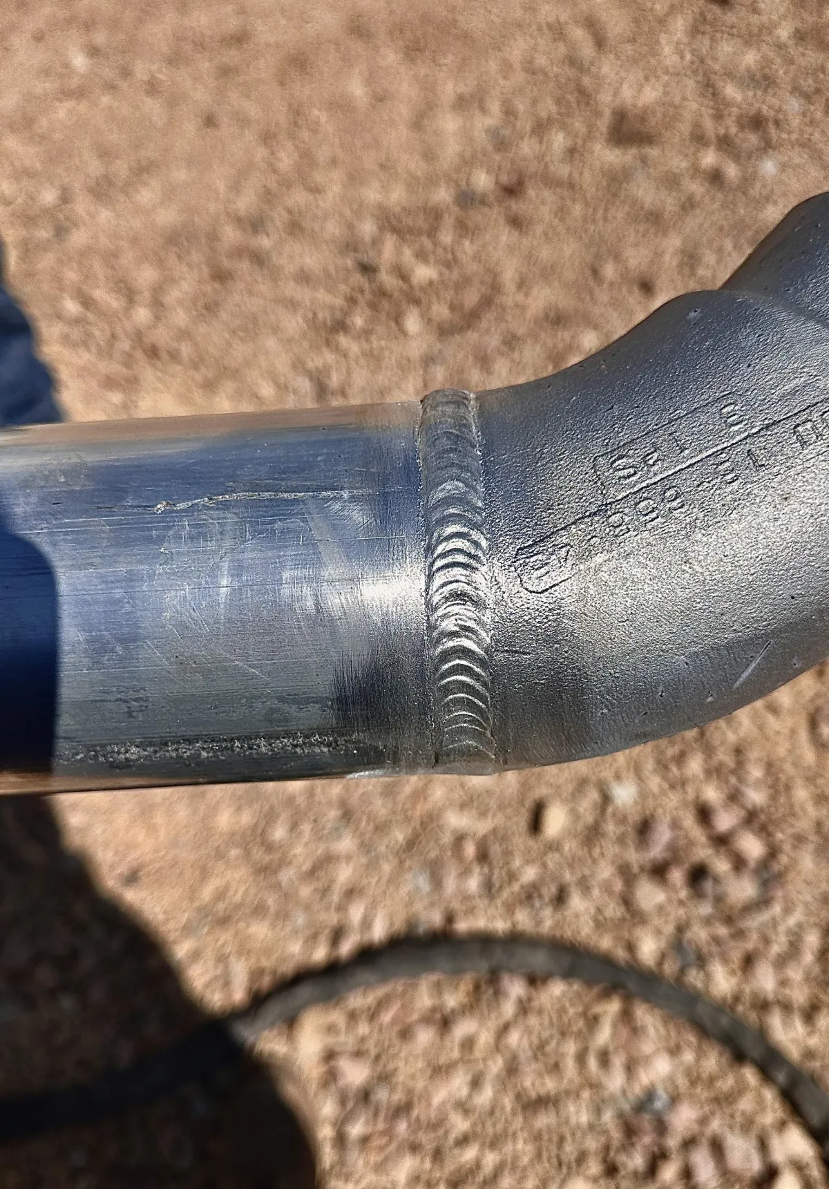 Close-up of an oil & gas pipe welding project showing a smooth, precise welded joint against a blurred gravel background.