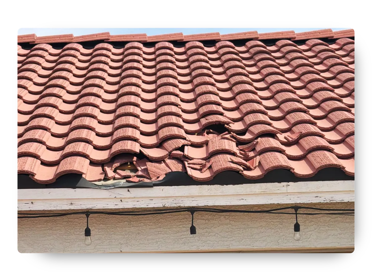 Severe tile roof damage along an eaves section requiring service from a roofing company near me.