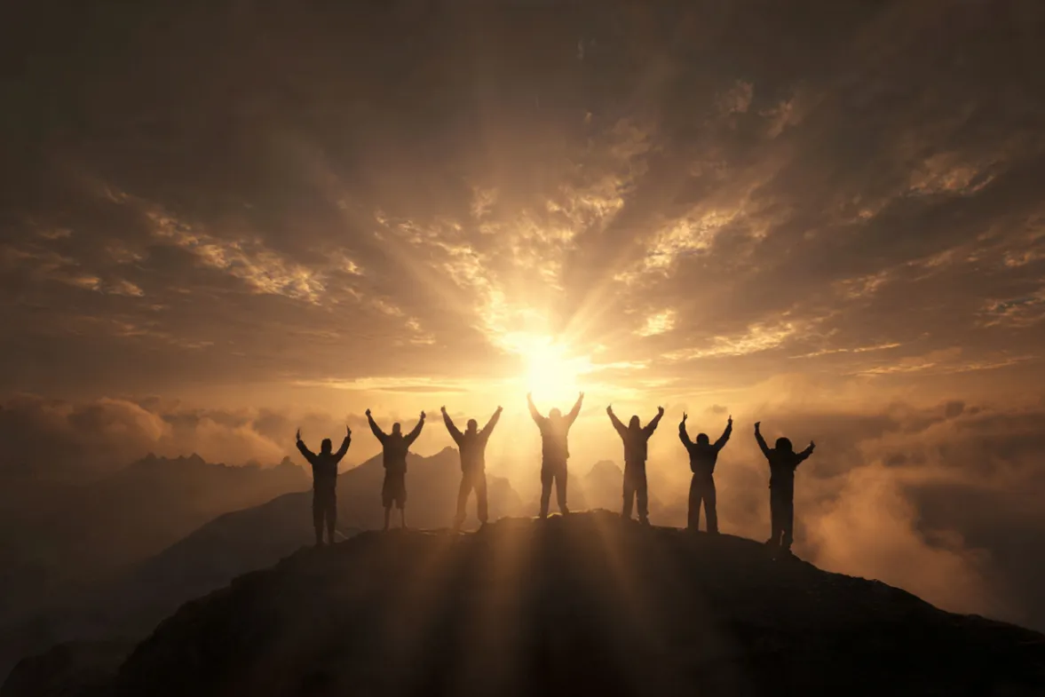 7 people standing on a mountain top above the clouds at sunrise