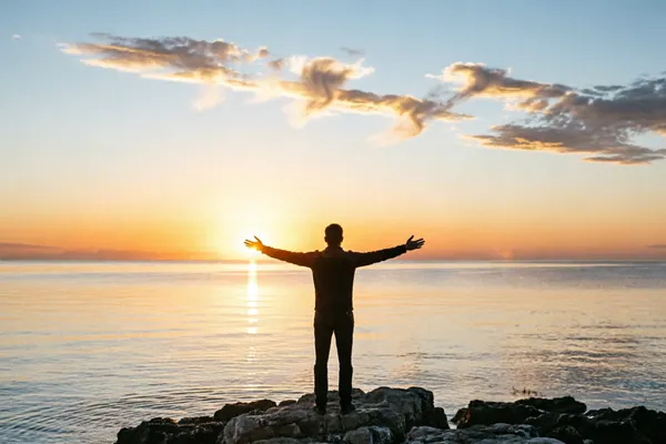 A powerful moment of connection with nature at dawn—a silhouetted figure with open arms against the radiant sunrise creates a deeply inspirational and uplifting scene.