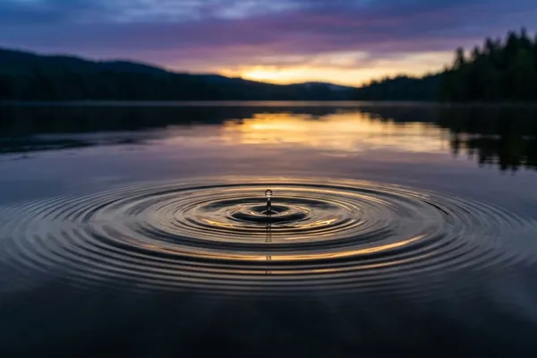 A single drop of water creates ripples on a calm lake at dawn, symbolizing the power of one small action / The Morning Motivator