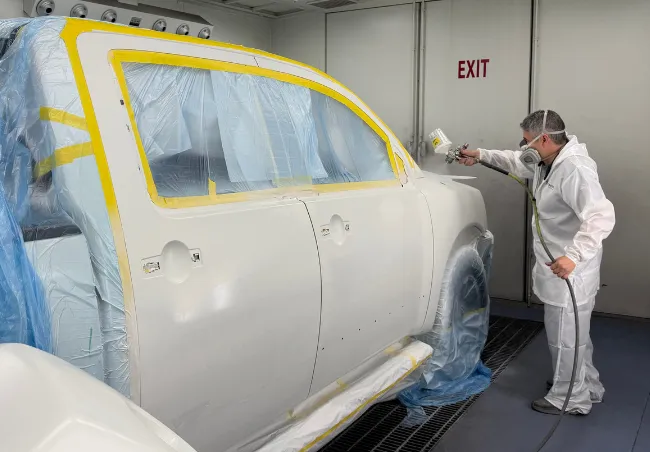 Professional painter spraying white paint on the front right fender and door of a truck