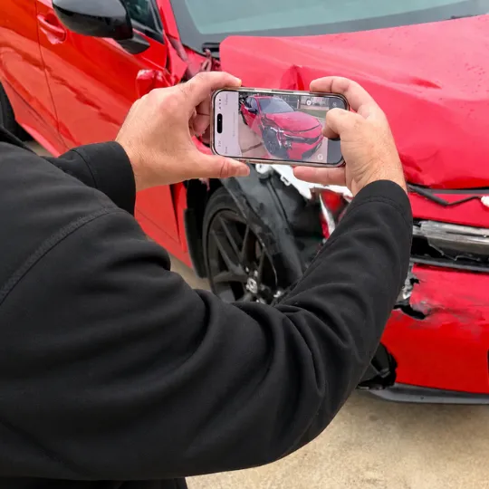 Man holding a cell phone and taking a photo of a wrecked red car to get an instant collision repair estimate