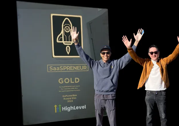 The photo about the Gohighlevel's SaaSPreneur award plaque and the cofounders, Blaine and Ronald raising their hands with smiles.