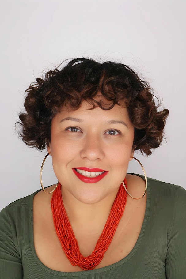 latina with short culry brown hair, hoop gold earrings, orange necklace, green top