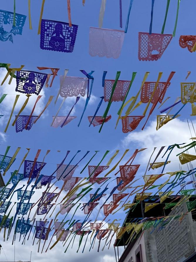 Colorful Papel Picado hung against a blue sky with white clouds