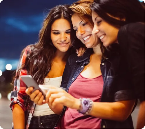 Three happy young women using a phone to book a rideshare