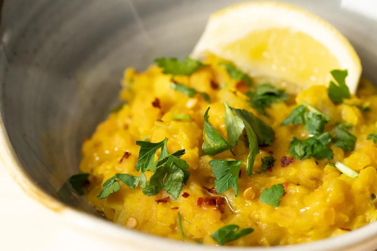 A bowl of lentil dhal with a lemon wedge and coriander on top, homemade whole food suitable for vegans