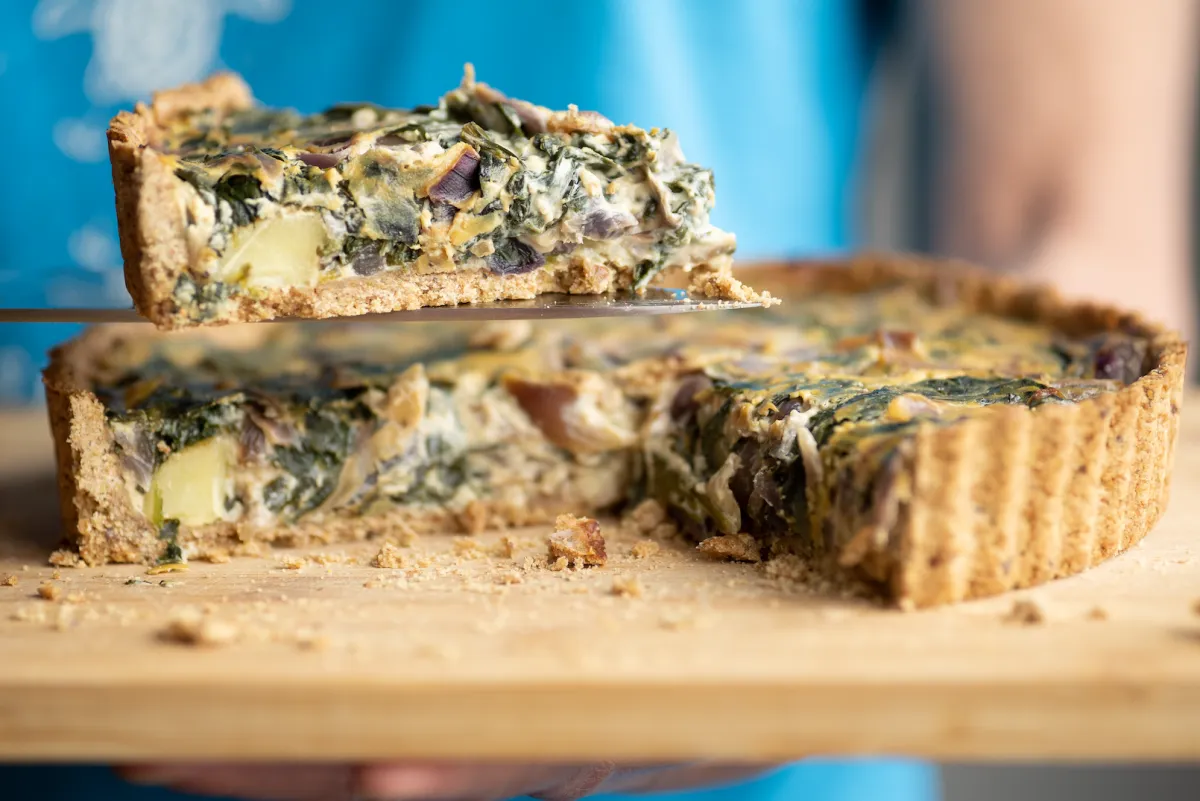 A woman holding a slice of spinach , red onion and potato quiche, made with wholemeal pastry; homemade whole food suitable for vegans