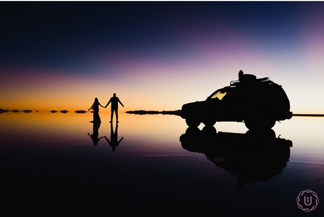 a couple of people sitting on a bench with a sunset in the background