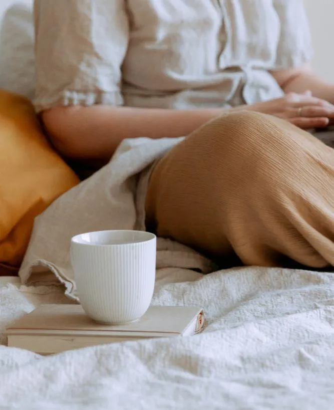 Torso of woman sitting in bed with laptop and cup of coffee