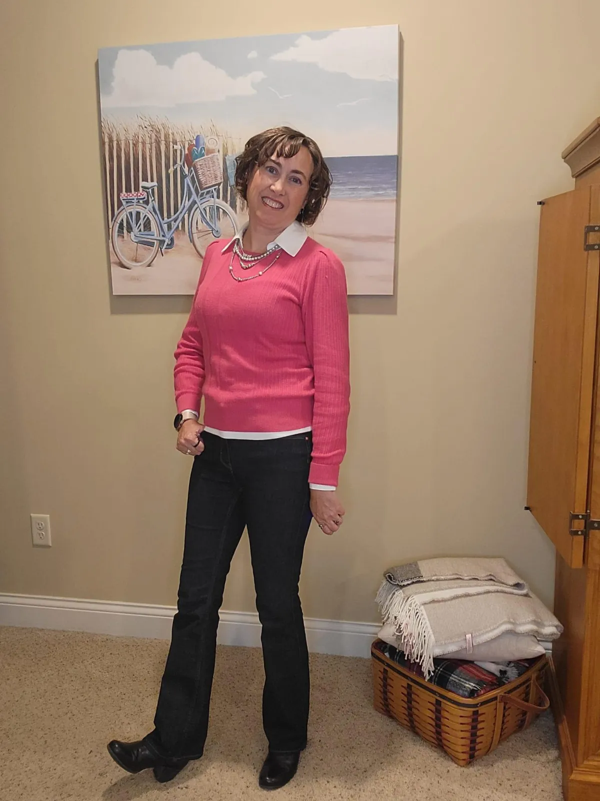 Jenn Whitacre wearing a WHBM pink cashmere-blend sweater layered over a white blouse with dark denim jeans, silver jewelry, and black boots. The blouse adds brightness at the neckline and hem, creating a soft yet refined look.