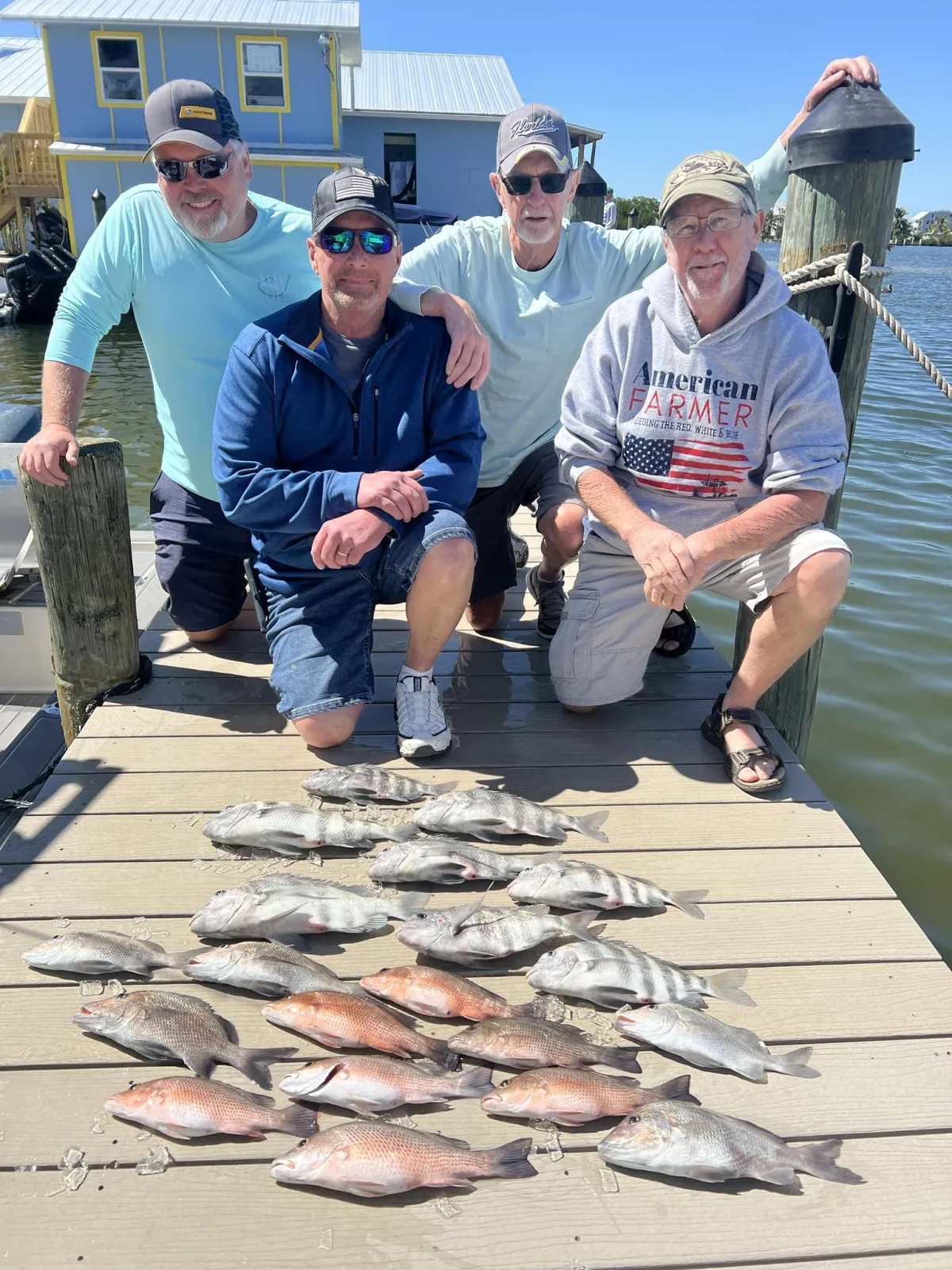 Captain Tanner and four smiling anglers pose on a dock beside a large catch of redfish and snapper, with colorful waterfront homes in the background on Pine Island, Florida.