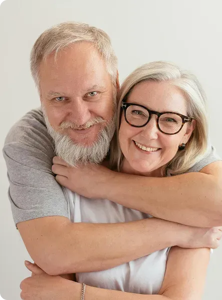 Happy mature couple smiling and hugging each other against a light background.