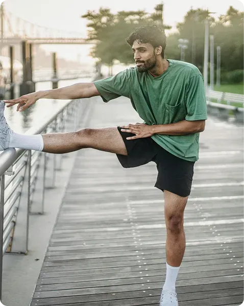 Man stretching his leg on a railing during an outdoor workout on a boardwalk.