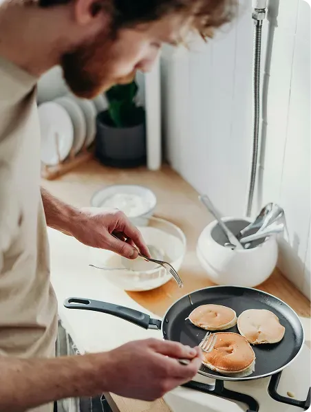 Man cooking pancakes in a kitchen, carefully flipping them on a pan.