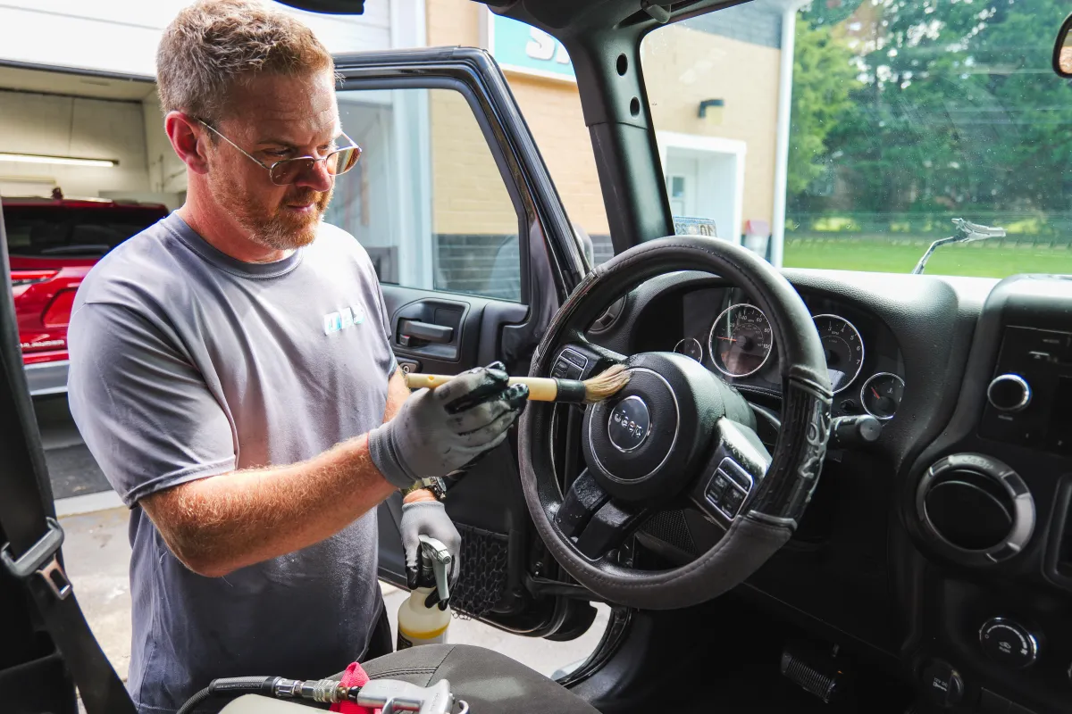 A detailer meticulously cleaning a Jeep steering wheel with a brush, showcasing interior mobile auto detailing Roanoke.