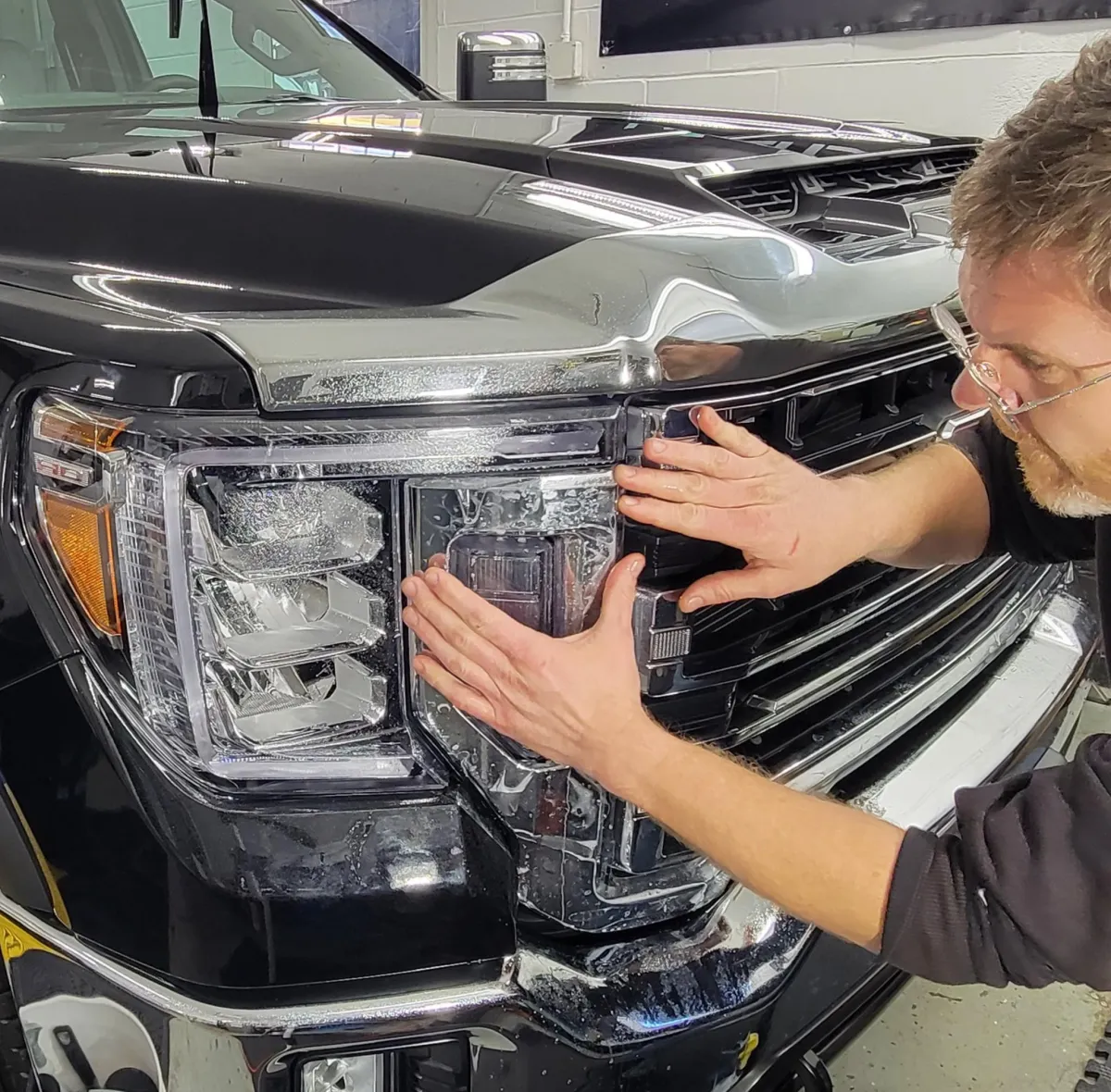 Expert applying a clear paint protection film to the headlight of a black truck in Roanoke for ultimate defense.