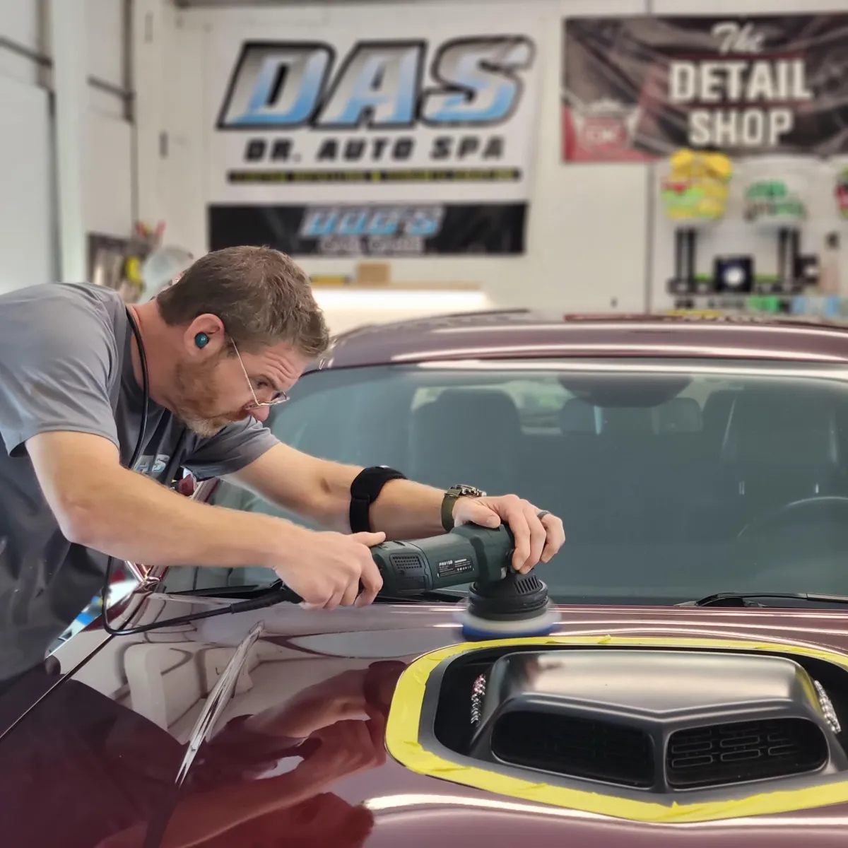 Professional performing paint correction on a maroon car's hood with a buffer at The Detail Shop in Roanoke.