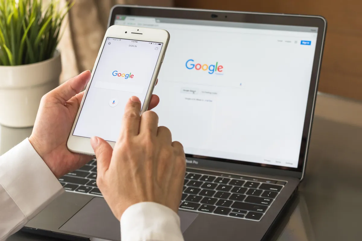 Pictureof man holding cell phones in front of laptop both screens how Google main page