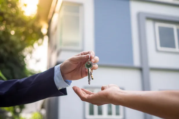 A man handing a key to a woman in front of a house - symbolizing the act of renting a building.