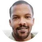 A smiling person with short dark hair is wearing a black and red striped shirt, standing in front of a beige background, reminiscent of a Google 5 star reviewer image.