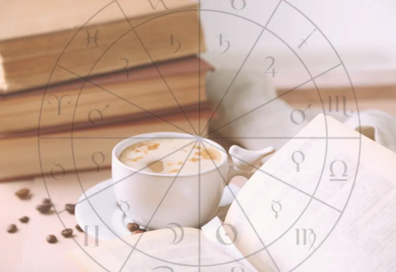 Open astrology book and birth chart notebook on a wooden desk beside a coffee mug — symbolizing reflection and self-discovery during an astrology reading.
